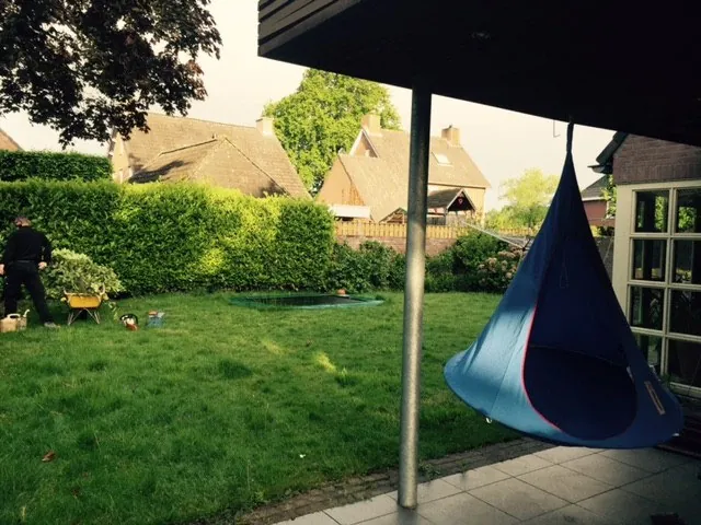 Blauwe hangende BRYCK Chair aan een frame boven het gras