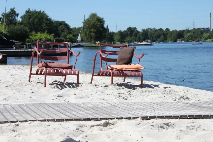 Twee roodgelakte stoelen op het zand aan de waterkant