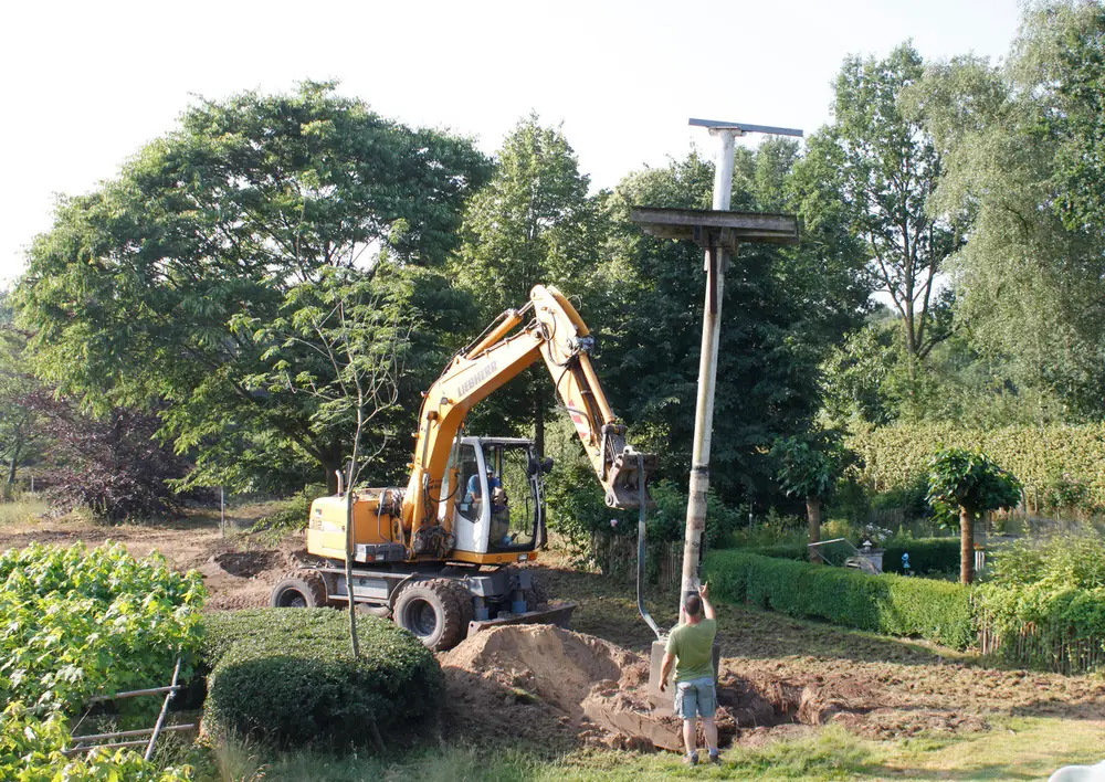 Graafmachine aan het werk in een open veld met bomen op de achtergrond