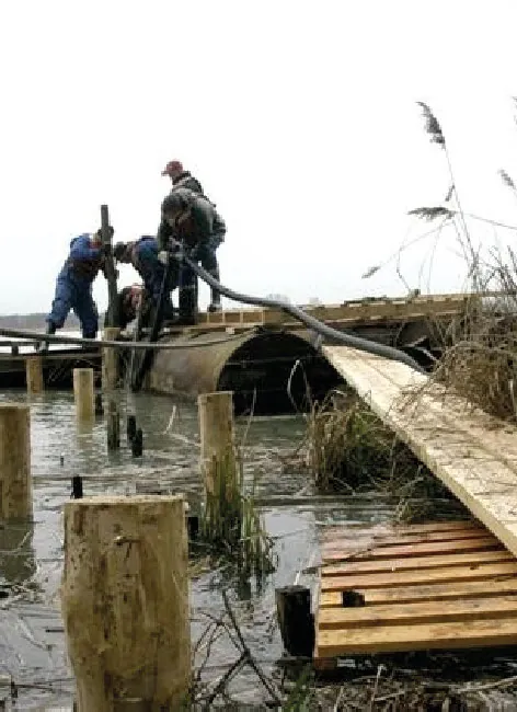 Twee mensen werken aan een houten vlonder aan de rand van het water