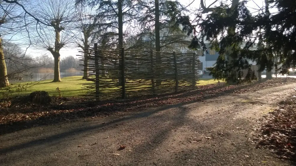 Zichtwand van takkenbossen tussen houten palen langs een grasveld