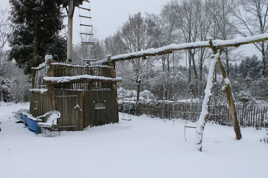 Besneeuwde tuin met een schommel en kale bomen in de winter