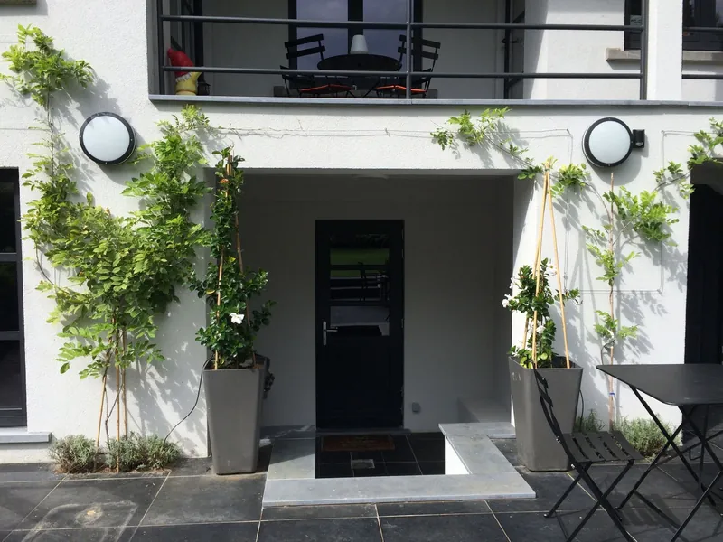 Witte gevel met klimplanten in hoge plantenbakken en een terras met bistrostoelen