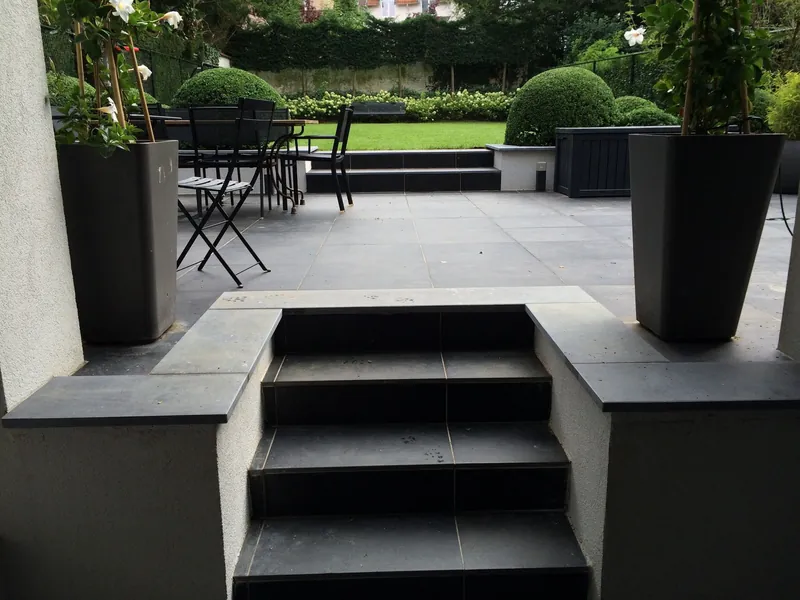 Terras met geschoren bollen in hoge donkere plantenbakken en een trap